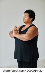 Vertical Portrait Of Black Senior Woman Meditating With Eyes Closed While Doing Yoga Indoors