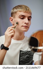 Vertical Portrait Of Blonde Young Man Using Face Massager While Filming Male Skincare Tutorial In Studio