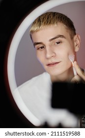 Vertical Portrait Of Blonde Young Man Using Face Massager While Filming Male Skincare Tutorial With Ring Light