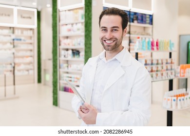 Vertical portrait of caucasian male young pharmacist druggist in white medical coat holding clipboard with side effects, active substance, prescriptions standing at pharmacy drugstore