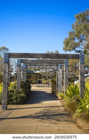 Vertical portrait composition looking down a timber pergola pathway surrounded by native grasses and trees at Bullion Park in Woodlea Estate, Aintree.