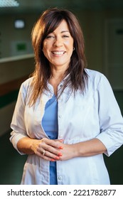 Vertical Portrait Of Confident Female Nurse At Hallway At Hospital. Dark Background.