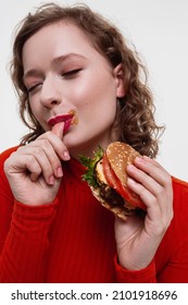 A Vertical Portrait Of A Curly Girl A Red Turtleneck Licking Finger After Eating Cheeseburger With Sauce Eyes Closed