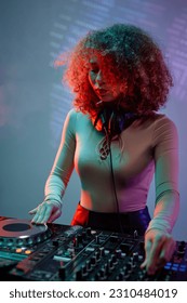Vertical portrait of curly haired young woman as female DJ making music in neon light - Shutterstock ID 2310484019