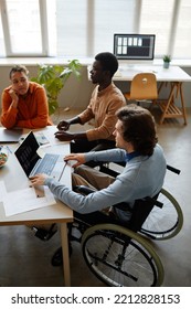 Vertical Portrait Of Diverse Business Team Discussing Project At Meeting Table Focus On Young Man Using Wheelchair In Foreground