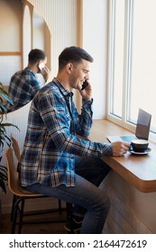 Vertical Portrait Of Fandsome Smiling Man 30 Years Old Talking On Phone And Working Remotely On Laptop In Cafe And Drinking Coffee