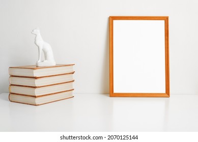 Vertical portrait frame mock-up with blank space for branding, picture, photo or text. Minimalistic interior template, empty frame, stack of books and indoor cat figurine. - Powered by Shutterstock