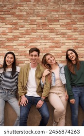 Vertical. Portrait group of cheerful friends posing together hugging looking smiling at camera. Happy generation z people leaning on brick wall outdoor. Relationships, friendship and community