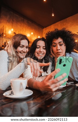 Vertical portrait of a group of young women having fun sharing media with an cellphone. Females looking the smartphone on a coffee shop. Girls shopping online on a marketplace using a mobile phone
