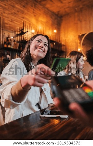 Vertical portrait of happy young woman paying bill with a contactless credit card in a restaurant. Cheerful female smiling holding a creditcard and giving a payment transaction to the cashier in a bar