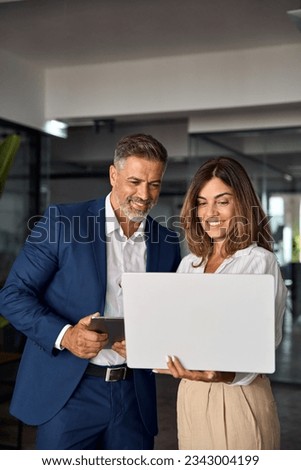 Vertical portrait of mature Latin business man and European business woman discussing project on laptop in office. Two diverse confident professional partners colleagues business people work together.