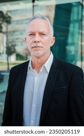 Vertical portrait of a mature serious business man with aexecutive suit, gray hair, and successful attitude looking pensive at camera. Confident male welldressed corporate worker standing at workplace