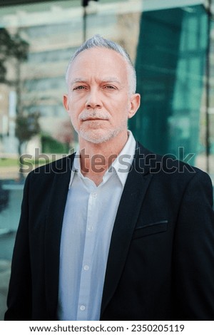 Vertical portrait of a mature serious business man with aexecutive suit, gray hair, and successful attitude looking pensive at camera. Confident male welldressed corporate worker standing at workplace
