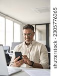 Vertical portrait of middle aged Hispanic business manager using cell phone mobile app. Smiling Latin or Indian mature man businessman holding smartphone sit in office working online on gadget.