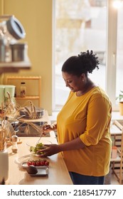 Vertical Portrait Of Overweight Black Woman Cooking Healthy Meal In Kitchen Lit By Sunlight