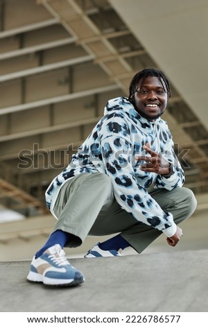 Vertical portrait of smiling black man wearing streetwear posing in urban area under bridge