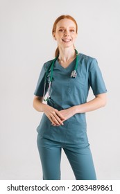 Vertical Portrait Of Smiling Young Female Physician In Medical Uniform With Stethoscope Around Neck Looking At Camera, Standing On White Isolated Background In Studio. Front View Of Positive Nurse.