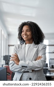 Vertical portrait of young African American leader manager, stands confident, crossed arms and looking aside in business office center. Portrait of professional business woman in stylish suit.