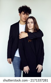 Vertical portrait of young attractive brown-haired man and woman in black clothes standing together, embracing. Male behind female, bound and love relationship couple. Studio shot on white background.