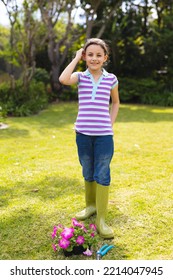 Vertical Portrait Of Young Caucasian Girl Wearing Striped T-shirt And Standing In The Garden. Spending Time Alone Outside Concept.