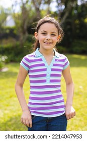 Vertical Portrait Of Young Caucasian Girl Wearing Striped T-shirt And Standing In The Garden. Spending Time Alone Outside Concept.