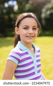 Vertical Portrait Of Young Caucasian Girl Wearing Striped T-shirt And Standing In The Garden. Spending Time Alone Outside Concept.