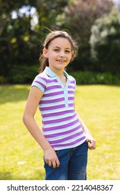 Vertical Portrait Of Young Caucasian Girl Wearing Striped T-shirt And Standing In The Garden. Spending Time Alone Outside Concept.