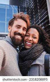 Vertical portrait of young multiracial couple. Man and woman tourist taking a selfie and smiling to the camera. Boyfriend and girlfriend having fun outdoors doing a portrait with smartphone. High - Shutterstock ID 2318208895