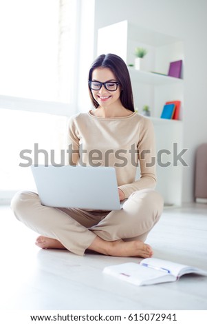 Vertical portrait of young pretty woman in glasses sitting on the floor at home and using laptop
