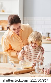 Vertical Portrait Of Young Woman Baking Cupcakes With Cute Little Boy Helping Mom In Kitchen Lit By Sunlight