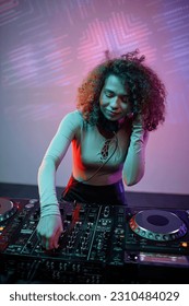 Vertical portrait of young woman as DJ making music tracks at disco party in neon light - Shutterstock ID 2310484029
