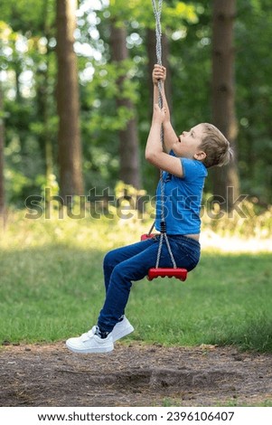 Vertical profile portrait of a little boy on a swing in nature. An ingenious child has invented a new way to spin by twisting the ropes of a swing.