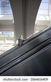 Vertical Profile Shot Of A Businessman Ascending On An Escalator In A Building.