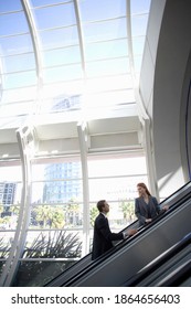 Vertical Profile Shot Of A Businessman And Businesswoman Facing Each Other On An Escalator Going Up In A Building.