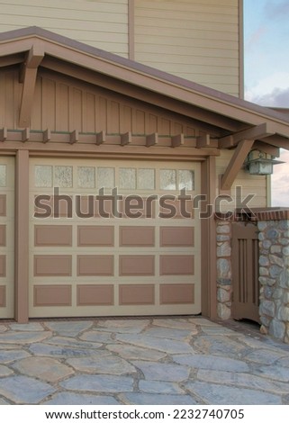 Vertical Puffy clouds at sunset Attached garage exterior with vinyl lap and stone veneer sidings at La Jolla in California. Traditional house with double garage doors with glass panels and concrete