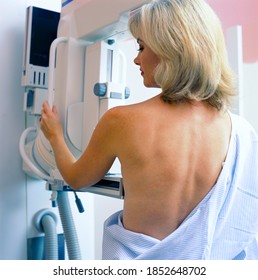 A vertical rear view of a woman in hospital gown taking a mammogram x-ray test in the clinic