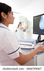 A Vertical Rear View Of A Woman Taking A Mammogram X-ray Test In The Clinic While Being Examined By A Professional Radiologist On A Monitor