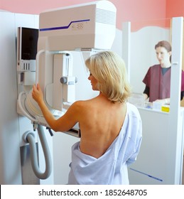 A Vertical Rear View Of A Woman Taking A Mammogram X-ray Test In The Clinic While Being Examined By A Professional Radiologist On A Monitor