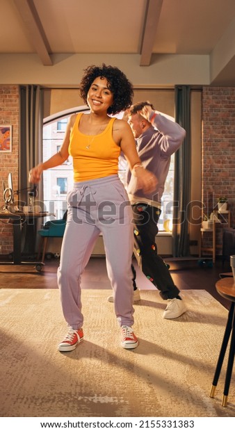 Vertical Screen: Happy Stylish Multiethnic Couple in\
Casual Outfits Recording a Dance Video from a Party at Home in Loft\
Apartment. Performing for Funny Viral and Active Video for Social\
Media App.