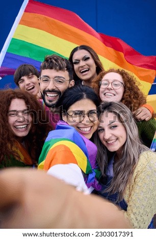 Vertical selfie of LGBT group of young people celebrating gay pride day holding rainbow flag together. Homosexual community smiling taking cheerful self portrait. Lesbian couple friends generation z.