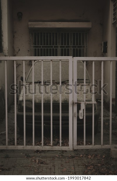 A vertical shot of an abandoned dusty car behind a\
low metal gate