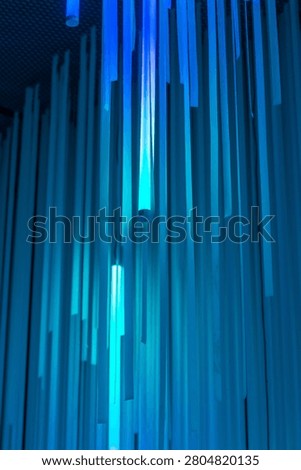 Vertical shot of an abstract geometric pattern with blue vertical panels illuminated by bright neon light tubes.