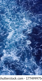 Vertical shot of an aerial view of sea foamy water, natural drawings, stains on clear blue water, beautiful sea background