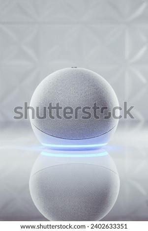 A vertical shot of Amazon Echo 4 with neon blue led light on the bottom part on the white table in background of shiny white textured walls