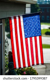 Vertical Shot Of An American Flag Hanging Vertically In Front Of A Business.