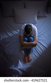 Vertical Shot Of An Anxious And Scared Young Man Sitting On His Bed At Night And Contemplating