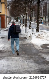 A vertical shot of the back of a man with a backpack walking on a snowy road