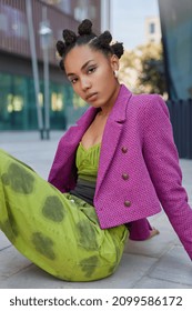 Vertical Shot Of Beautiful Dark Skinned Serious Woman With Hair Buns Dressed In Fashionable Clothes Poses Outdoors Against Urban Background. Street Photography. People Style And Lifestyle Concept