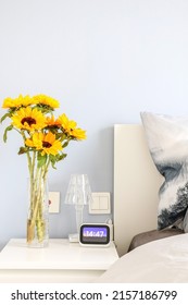 Vertical Shot Of Beautiful Natural Yellow Sunflowers (Helianthus) In A Glass Vase On Bedside Table Freshening Up Elegant And Modern Bedroom Interior, 14:47 On The Digital Clock