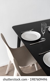 Vertical shot of black matt kitchen table with dinner set up, view from above. White dinnerware, wineglasses and cutlery in minimalistic black and white interior design